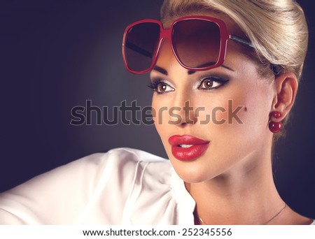 Portrait of beautiful blonde woman in sunglasses and red plump lips on dark background with copyspace
