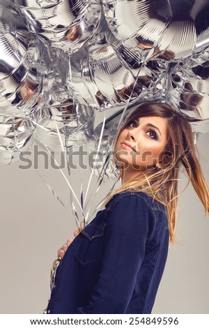 Beautiful dreaming teenager girl posing in blue jeans shirt with ombre hair and silver balloons in her hands