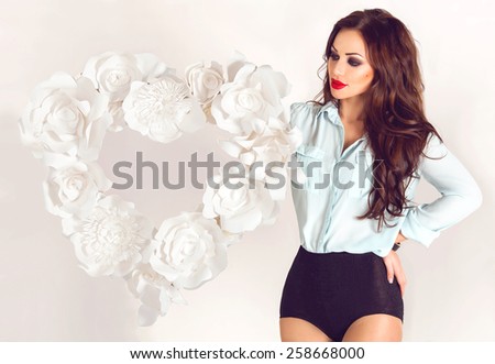 Sexy brunette girl in blue blouse and vintage black panties standing near white heart frame border made of paper flowers