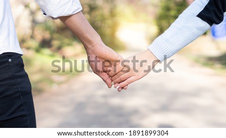 The hands of the male and female lovers who hold hands walk forward high with blurred background