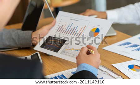 Picture of two young businessmen at a meeting Analyzing the financial markets, the youngster works in the office on his laptop while sitting at a wooden desk and analyzing the documents in hand. finan Imagine de stoc © 