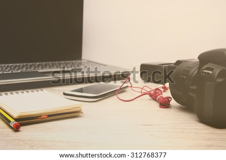 Laptop, digital camera, mobile phone, notebook and earphones on wood table. Old style