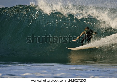 A surfer in a wetsuit glides through a perfect tube on a beautiful green wave.