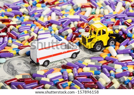 Bulldozer clears the way for the ambulance through the dollars and pills (installation on the theme of modern medicine trends)