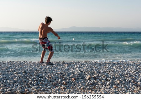 Teenager boy throwing stones into sea