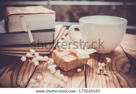 Books, flowers, white cup and wrapped gift box on wooden table. Toned image