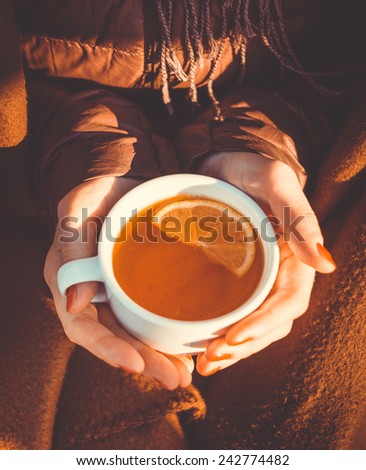 Cup of hot tea with lemon  in hands in cold winter sunny day. Toned picture