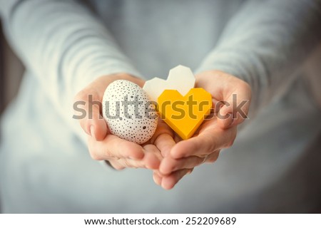 Hands holding modern painted easter egg and paper hearts. Toned picture