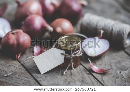 Red onion marmalade in a small glass jar on wooden table. Blank label provides copy space for a message. Toned image