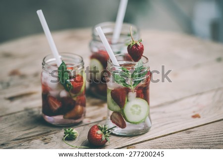Three retro glass jars of lemonade with  strawberries, cucumber and mint on wooden table. Toned image