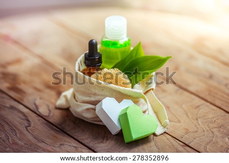 Cosmetic bottle containers with green herbal leaves in small organic cotton bag on wooden background
