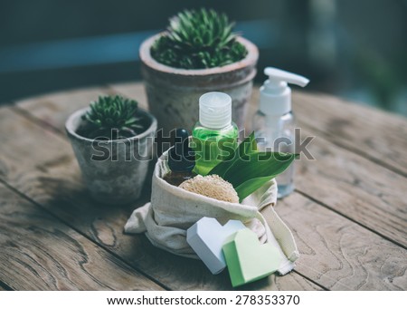 Cosmetic bottle containers with green herbal leaves and garden pots with flowers on wooden background. Toned image