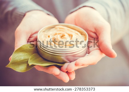 Cosmetic cream container with green herbal leaves in woman hands. Toned image