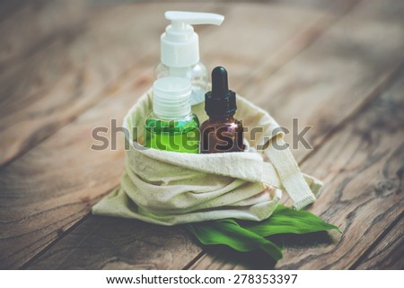 Cosmetic bottle containers in small organic cotton bag with green herbal leaves on wooden background. Toned image