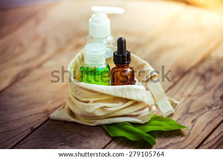 Cosmetic bottle containers in small organic cotton bag with green herbal leaves on wooden background