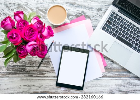 Bouquet of roses, cup of coffee, female hands with tablet and laptop on old wooden table. Top view