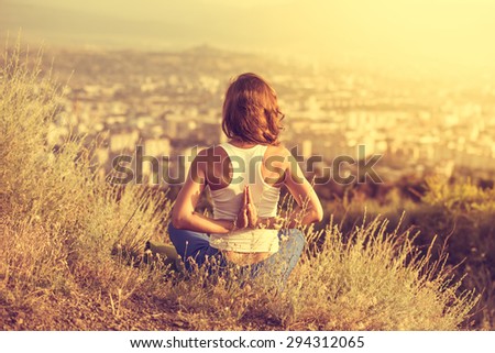 Young woman sits in namaste yoga pose with city on background. Freedom concept. Calmness and relax, woman happiness. Toned image