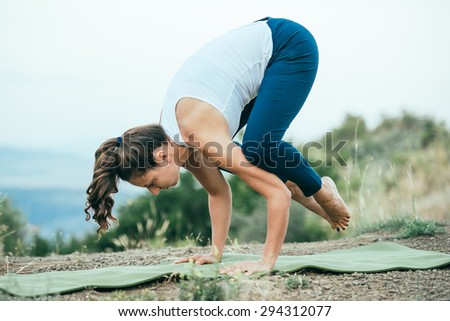 Young woman practicing yoga outdoor in the nature with city on background