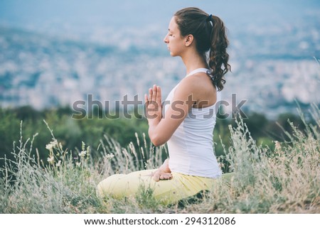 Young woman sits in yoga pose with city on background. Freedom concept. Calmness and relax, woman happiness. Toned image