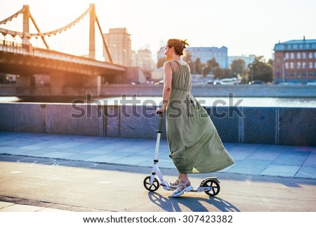 MOSCOW, RUSSIA - AUGUST 9, 2015: Young woman is riding scooter in Muzeon park near Krymsky (Crimean) bridge at sunset in Moscow, Russia. Toned image