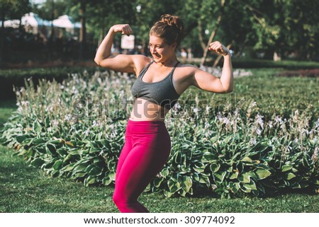 Strong fitness woman showing biceps muscles strength in park. Toned picture