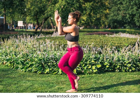 Young woman practicing yoga in Eagle (Garudasana) pose in park