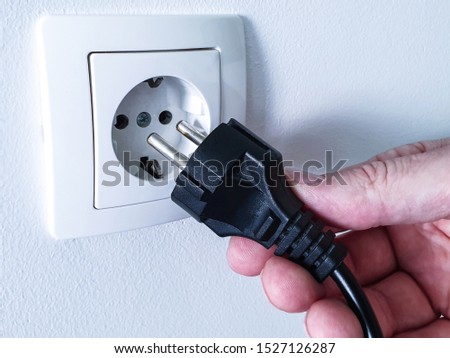 Connecting black electrical power plug with a hand inside a white plastic power socket on a white wall 商業照片 © 