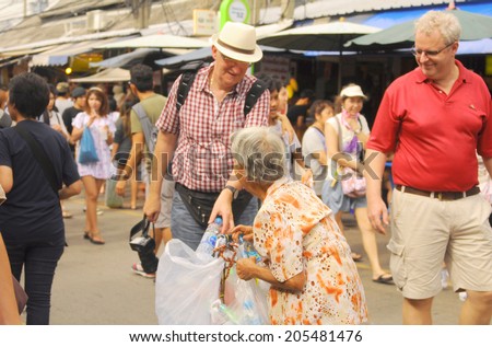 Bangkok - circa June 2014 - an unidentified foreign tourist gives a bottle to an old woman. She keeps a plastic bottle to sell to recycle shop, JJ market, Bangkok