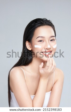 Beauty portrait image of pretty asian woman smiling and applying face cream isolated over light grey background Stock foto © 