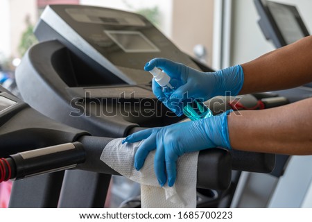 Staff using wet wipe and alcohol sanitizer spray to clean treadmill in gym. Antiseptic,disinfection ,cleanliness and heathcare , anti virus concept. Anti Corona virus (COVID19).Selective focus.