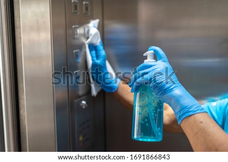 Closeup of old staff hand using wet wipe cleaning an elevator push button control panel with a blue sanitizer bottle.Disinfection,cleanliness and healthcare,Anti Corona virus,COVID-19.Selective focus.
