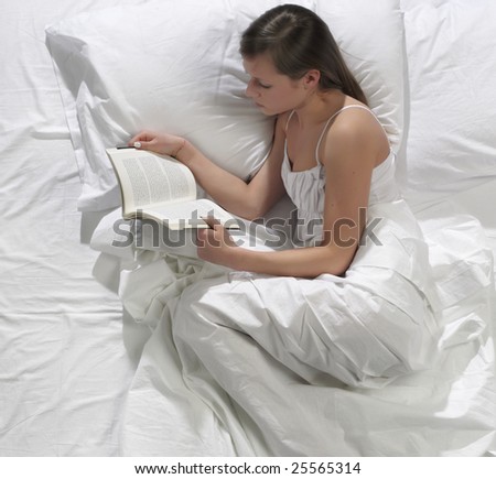 A pretty young woman reads a book in bed