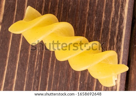 One whole yellow pasta fusilli macro flatlay on brown wood 商業照片 © 