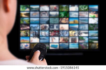 Online Multimedia video concept on TV set in dark room. Woman watching online TV with remote control in hand. Multimedia streaming VoD content provider concept.