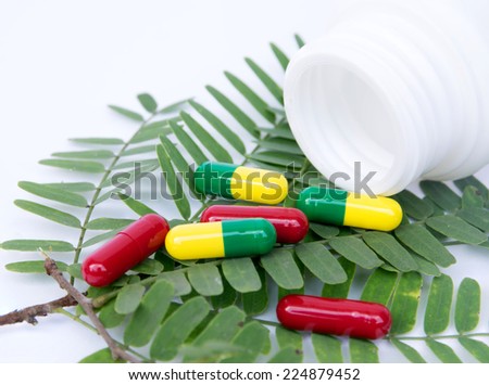 herb capsule spilling out of a bottle above left herb on white background
