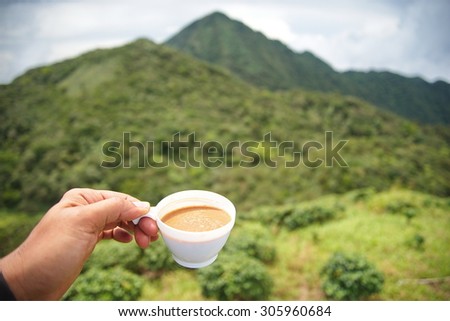 a cup of coffee in hand with mountain is background