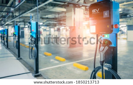 Blurred electric car charging station for charge EV battery. Plug for vehicle with electric engine. EV charger. Clean energy. Charging point at car parking lot. Future transport technology.