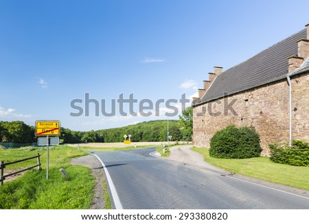 A country road leading past farm buildings fortified like a small castle in the North Eifel, Germany