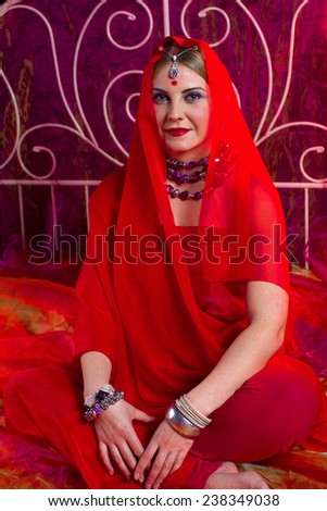 portrait of a young woman in the Indian manner, in red colors, black background, blonde, on the bed, her hair covered with a handkerchief