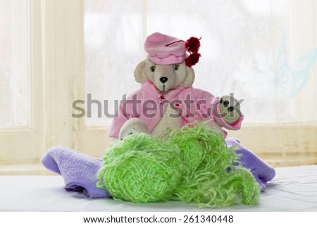 teddy bear in pink blouse and pink beret with red pom-poms on the background of bright windows, a bright sunny day and a festive spring mood. Tangles and threads,