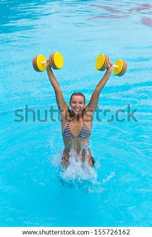 Woman is engaged aqua aerobics with dumbbells in water