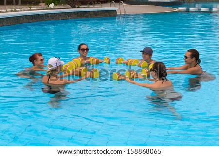 Happy active fitness people doing exercise with aqua dumbbell in a swimming pool