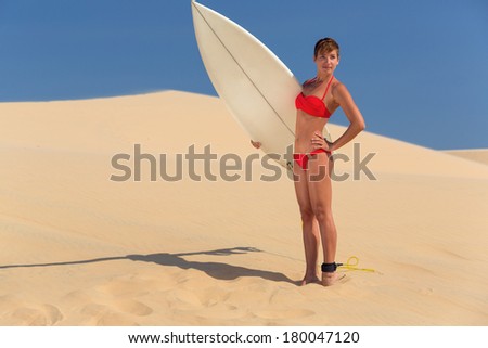 Rear view of sexy beautiful young woman surfer girl in bikini with white surfboard at a beach