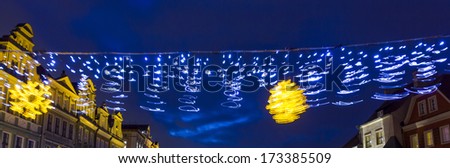 Blurred christmas decorations in a city square with historical buildings and night sky in background