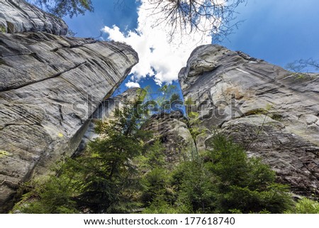 wide angle photo of towering rocks and trees against the background of blue sky with white clouds, Adrspach, Czech Republic
