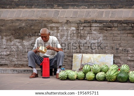 Pingyao, China - July 26, 2009: A watermelon street seller eats his lunch on July 26, 2009. Pingyao ancient town is one of the greatest attractions of Shanxi province.