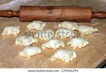 Homemade dumplings lying on plank prepared for cooking on kitchen board with rolling pin