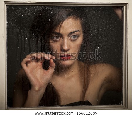 Beautiful girl looks out of the window with raindrops.