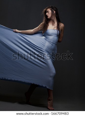 Beautiful young girl dancing with blue fabric on a gray background.