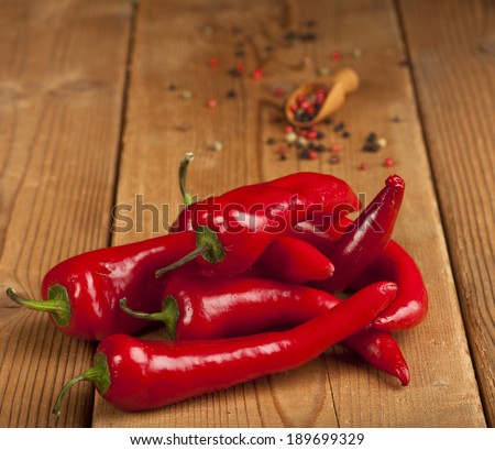 Red Hot Chili Peppers and spoon with grains of black, green and red pepper over wooden background.